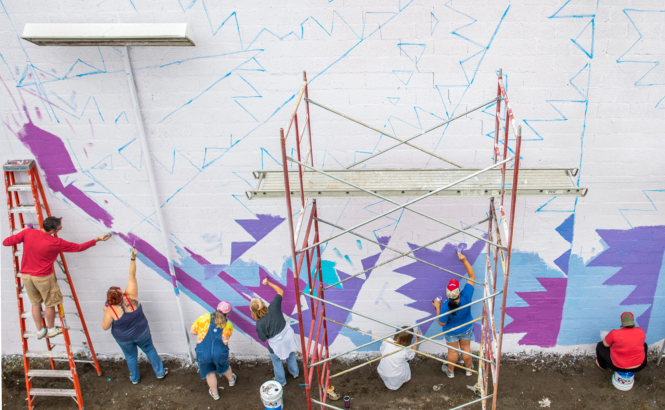 A group of people painting a blue and purple mural on a white wall. 