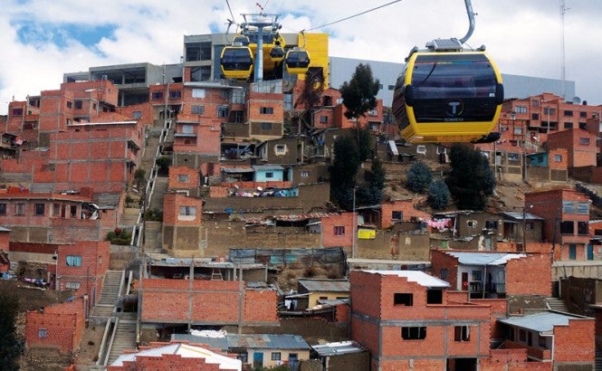 Teleféricos aéreos amarillos viajan por una colina en América Latina sobre asentamientos informales hechos de ladrillos. Crédito: Gwen Kash