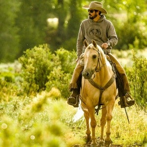 Colorado rancher Paul Bruchez rides a horse in a green field. 