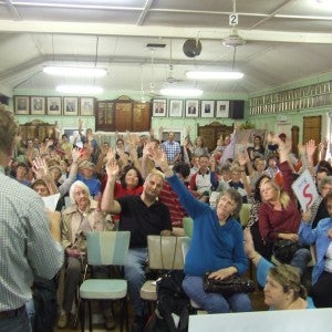 People in a meeting in a classroom with hands raised