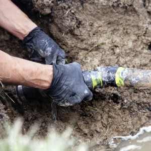 A pair of hands are seen repairing a broken pipe