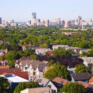 An aerial photo of houses and trees with an urban skyline in the background