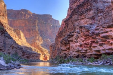A river runs throuh a deep canyon made of reddish rock.