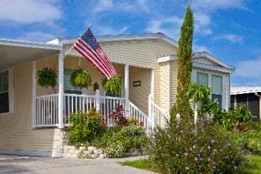 Manufactured home Front entrance image of one-level manufactured home with garden and United States flag.