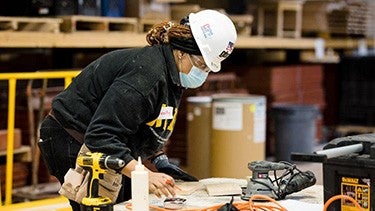 Wood worker measuring wood Masked woodworker with hard hat at a table measuring wood in a work site