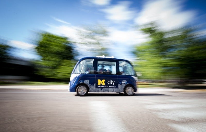 A driverless shuttle at the University of Michigan in Ann Arbor, where researchers are studying consumer acceptance of autonomous vehicles. Credit: Levi Hutmacher, University of Michigan This image shows a street with a blue driverless shuttle in the middle. Blurred trees sit in the background of the image.