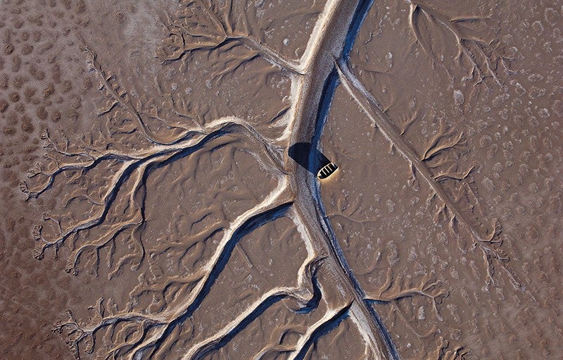 Fishing boat in the Colorado River Delta. Credit: Pete McBride. Aerial view of a fishing boat stranded on a brown and dried up Colorado River Delta.