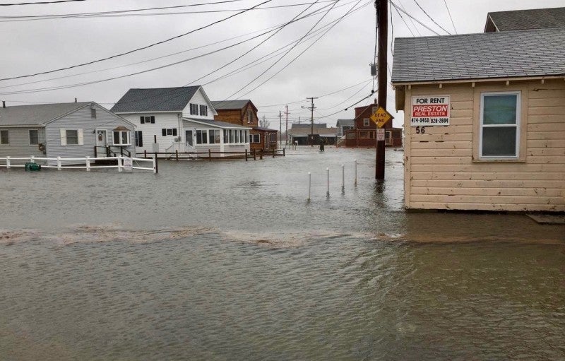 At least a foot of water floods a neighborhood of single family houses, with a cloudy sky in the background.