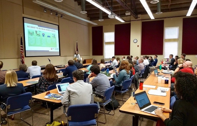 Credit: Janae Futrell 40 conference participants sit at desks looking at a power point presentation during the second annual Consortium for Scenario Planning Conference.