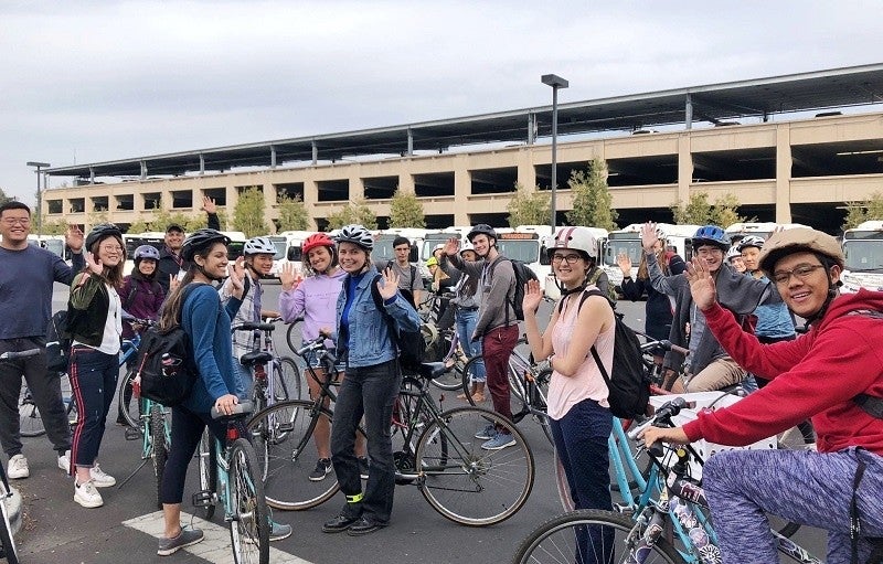 A group of students poses with their bikes in the middle of a bike tour.