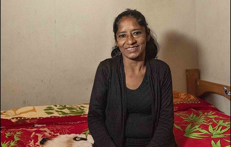 Una mujer, sentada en una cama, sonríe.