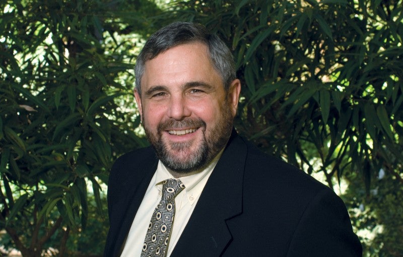 A photograph of the head and shoulders of a smiling man, George W. McCarthy, in his middle years wearing a dark suit and tie against a leafy background. 