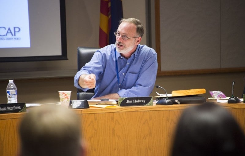 Jim Holway speaks in front of an audience, gesticulating enthusiastically with his right hand.