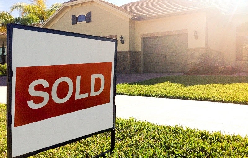 Implementing targeted taxes such as transfer fees on high-end real estate can be alluring to municipalities, but experts warn that these moves can backfire. Credit: www.aag.com via Flickr CC BY 2.0. A "sold" sign sits on a front lawn in front of a large home.