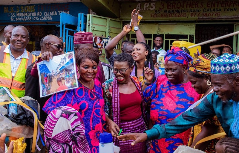 A group of people in brightly colored clothing smile at the camera outside.