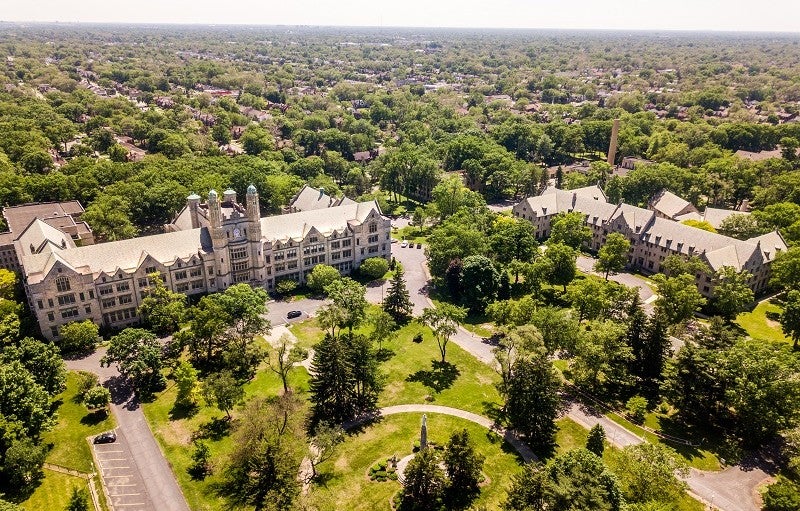 Marygrove College y el vecindario Livernois-McNichols. Crédito: Jordan Garland, cortesía de la Fundación Kresge. 260/5000 La fotografía muestra una vista aérea del campus lleno de árboles de Marygrove College y el vecindario circundante. Los dos edificios más visibles en el campus son viejos, grandes y de piedra clara con muchas ventanas con paneles de plomo. Uno de los edificios tiene una torre de reloj.