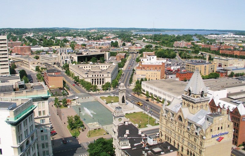 Mayor Walsh advocates replacing the elevated section of Interstate 81 running through Syracuse with a ground-level transition into the city’s street grid. Credit: City of Syracuse. Aerial view of Syracuse showing a municipal park and buildings, with and elevated section of Interstate 81 in the distance
