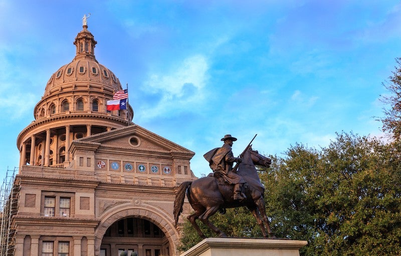 TriciaDaniel/iStock/Getty Images A sand-colored building with a domed roof stands on the left with trees on the right and a statue of a man on a horse in the foreground.