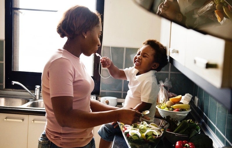 A woman feeds a toddler in a kitchen.