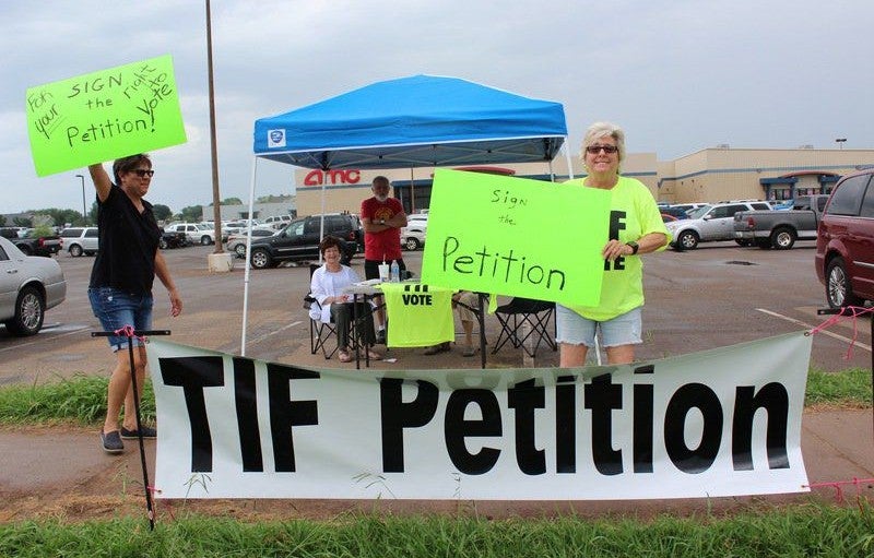 People hold neon green signs behind a large white banner reading TIF Petition in black letters.