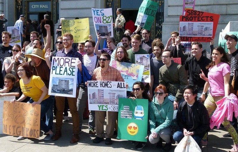 A group of YIMBY advocates pose for a picture with signs supporting California bill SB 827. 